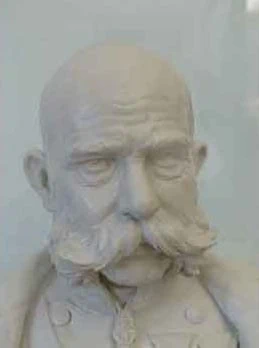 Eine Gipsbüste eines älteren Mannes mit markantem Schnurrbart, Glatze und Uniform. Die Skulptur weist detaillierte Gesichtsausdrücke und Texturen auf und fängt eine ernste oder nachdenkliche Haltung ein.
