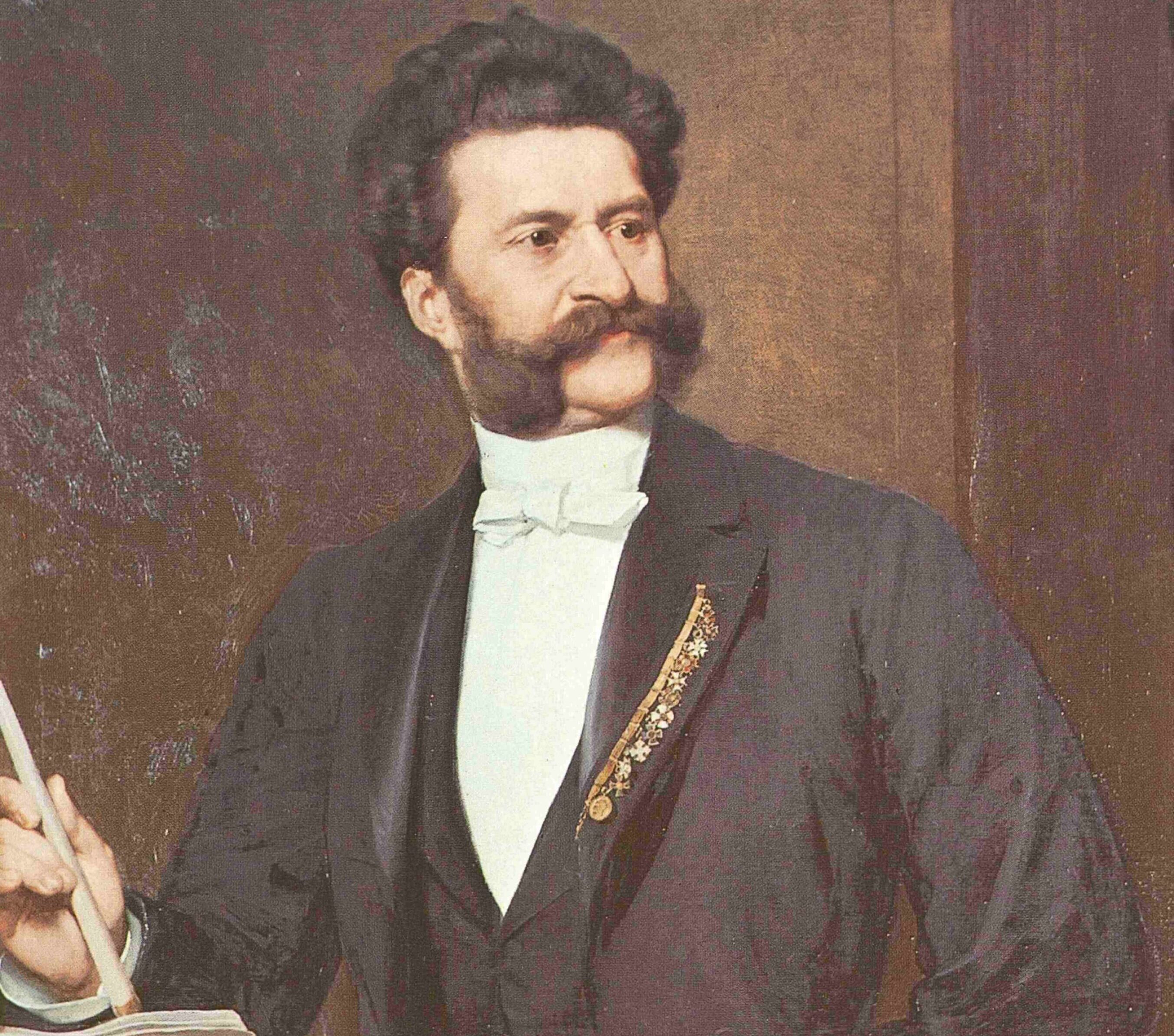 Johann Strauß – eine musikalische Revolution. Ein Mann mit dunklem Haar und großen Koteletten trägt einen formellen schwarzen Anzug mit weißem Hemd und Fliege. Er steht mit einem Taktstock in der Hand an einem Podium und scheint zu dirigieren oder eine Rede vor einem Publikum zu halten.