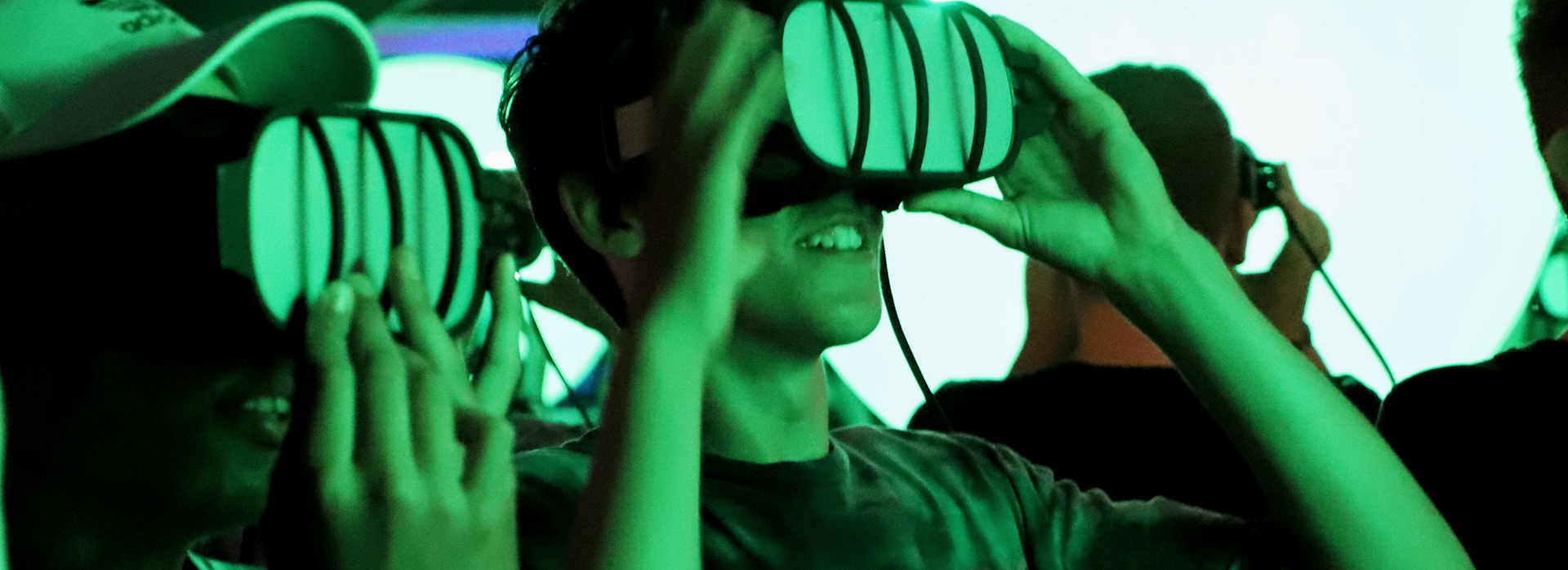 Eine Gruppe von Menschen, die Virtual-Reality-Headsets tragen, lächeln und in einer hell erleuchteten, grün getönten Umgebung interagieren.