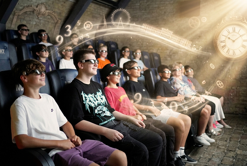 A group of people, mostly children, wearing 3D glasses sit in a theater, smiling and looking ahead. Above them, luminous dials and numbers swirl through the air, creating a magical time travel atmosphere. 