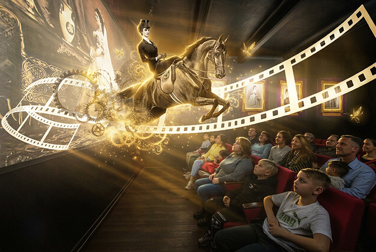 A group of people in a theater watch an impressive 3D show in which a glowing film reel and a woman on a horse appear to jump out of the screen, surrounded by golden lights and visual effects.