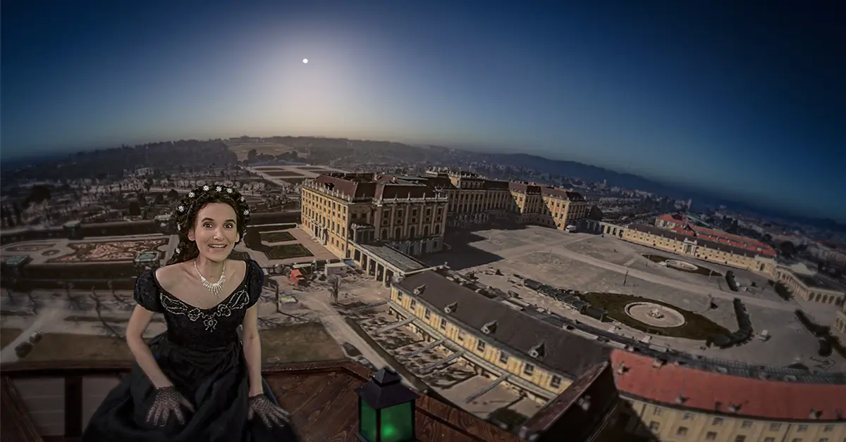 Eine Frau in einem schwarzen Kleid mit einer Tiara sitzt unter der strahlenden Sonne und einem klaren blauen Himmel auf einem Balkon mit Blick auf das prächtige Schloss Schönbrunn und seine Gärten in Wien, Österreich.
