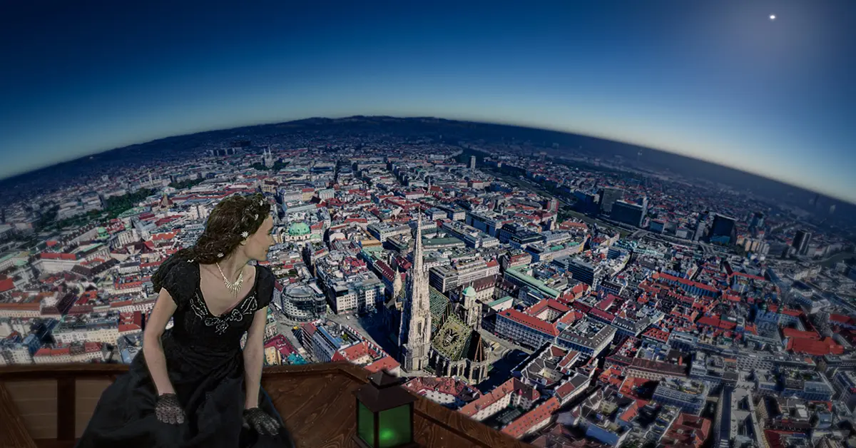 Eine Frau in einem schwarzen Kleid sitzt auf einem Balkon und überblickt eine weite Stadtlandschaft mit Gebäuden mit roten Dächern unter einem tiefblauen Himmel, darunter ist eine markante Kathedrale zu sehen.