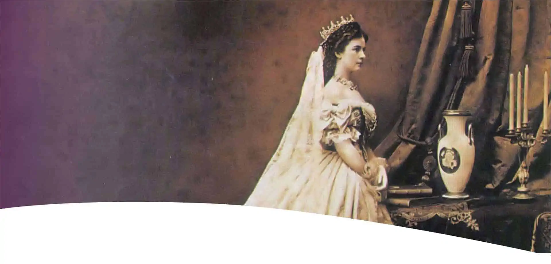 Eine Frau in einem eleganten historischen Kleid und mit Krone steht an einem Tisch mit einer Vase, Büchern und einem Kandelaber und blickt vor einem sepiafarbenen Hintergrund nachdenklich nach rechts.