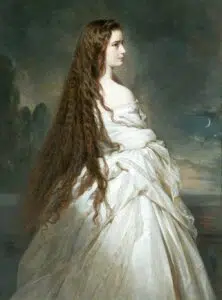 Žena s velmi dlouhými vlnitými hnědými vlasy stojí z profilu v elegantních bílých šatech. Pozadí je tmavé a atmosférické, se stromy a půlměsícem.